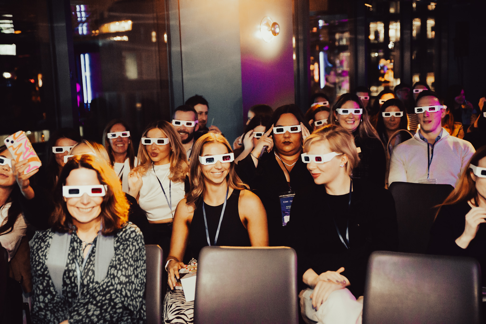 Attendees of the event smile at the camera. There are several dozen people, and they are all wearing red-and-blue lens 3d glasses