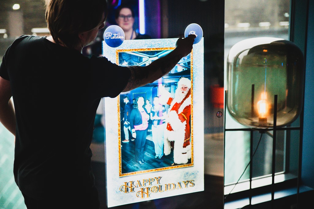 Social Jungle's AR Santa experience being tested at the event: a large screen shows two attendees 'with' santa. A Social Jungle employee is tapping a button on the screen.